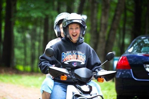 Two people ride on a scooter with helmets.