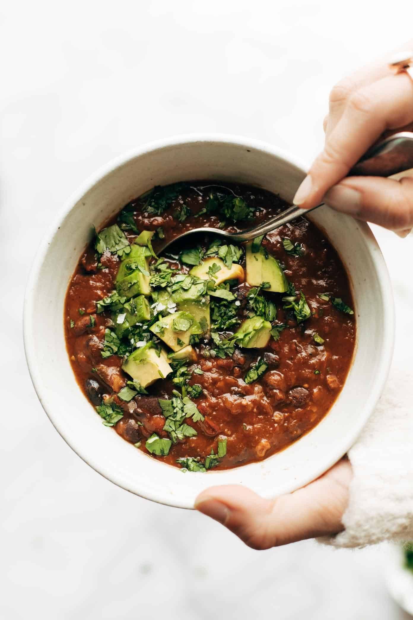 A person reaches into a bowl of chili with a spoon.