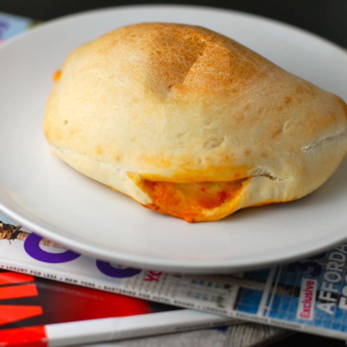 Sausage and mozzarella calzone on a white plate on top of magazines.